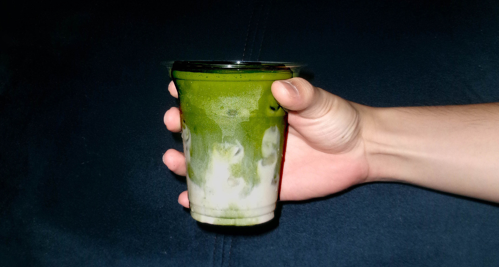 A hand reaching for a layered iced matcha latte on a stone ledge at night